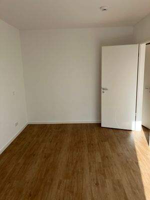 Weitere Ansicht des Schlafzimmers mit weiß angelegten Wänden und braunem Vinylboden in Holzoptik