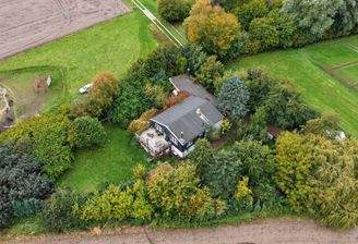 Schräge Luftaufnahme von Haus, Holzterrasse und Baumgarten mit Feldumfeld