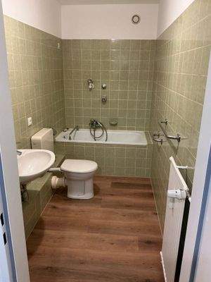 Badzimmer mit Bodenbelag in Holozoptik und grünen Wandfliesen