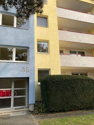 Eingangsbereich des mehrstöckigen Wohngebäudes umgeben von Grünanlagen mit Bäumen und Sträuchern