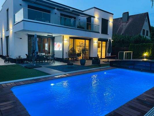 Außenanlagen mit beleuchtetem Pool und Haus im Hintergrund