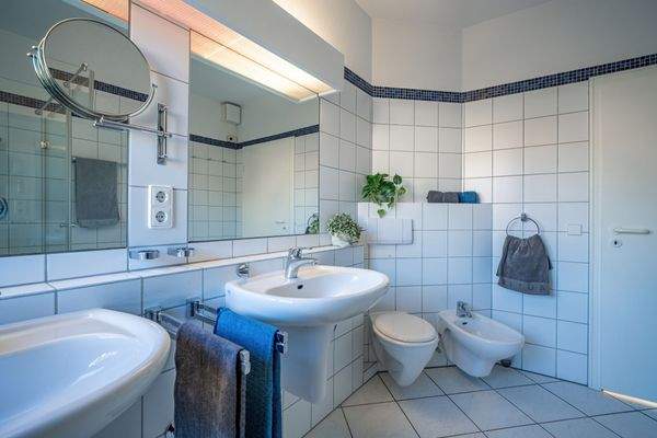 Der Raum ist klassisch weiß gefliest und mit zwei Waschbecken ausgestattet.