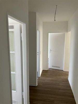 Flur mit Fußboden in Holzoptik, Blick in den Gang, links Eingang zur Küche, geradeaus Eingang zum Zimmer, weiße Türen 