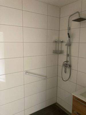 Barrierefreie Dusche, Duschgarnitur mit Regendusche, weißen Wandfliesen und dunkelgrauen Bodenfliesen