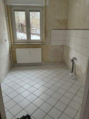 Küche mit Fenster mit tapezierfähigen Wänden und hellem Fliesenspiegel. Es ist ein PVC-Boden in Holzoptik verlegt.