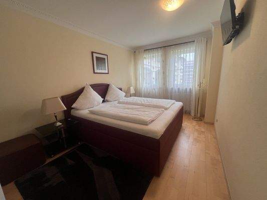 Gemütliches Schlafzimmer mit Doppelbett, seitlichen Nachttischen und TV an der Wand