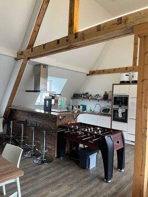 Küche und Aufenthaltsraum mit Kochinsel, Barhockern, voll ausgestatteter Küchenzeile und Tischkicker in der Mitte.