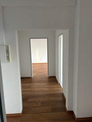 Flur mit Blick Richtung Wohnzimmer, weiß angelegte Wände, brauner Vinyl-Designboden