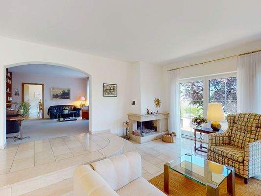 Lichtdurchfluteter Wohnbereich mit Kamin und Zugang zur Terrasse.