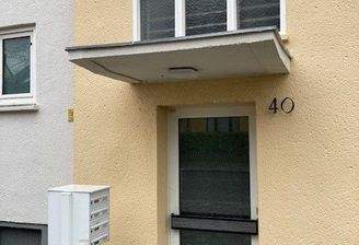 Blick auf den Hauseingang des gelben Hauses mit weißer Glaseingangstür und Wohnungsfenster