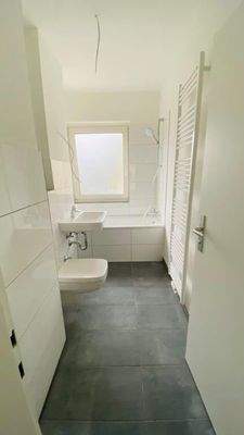 Badezimmer mit Badewanne, weiß gefliest und dunklem Fliesenboden.jpg