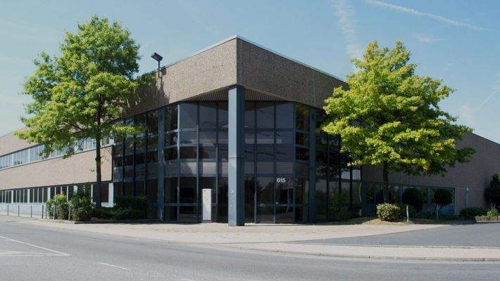 Moderne Gewerbeimmobilie mit Flachdach, großen dunklen Glasflächen und vorgelagerten Bäumen an einer Straßenecke.