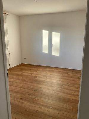 Blick in das Schlafzimmer mit braunem Vinylboden. Wände und Decke weiß angelegt.