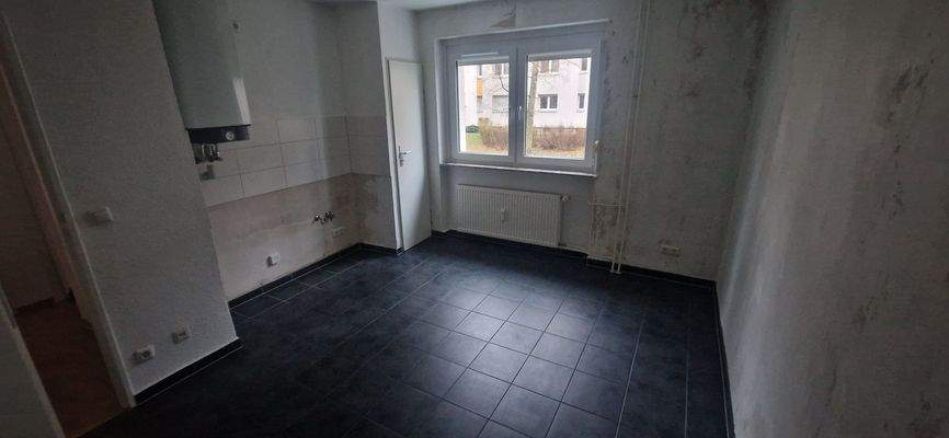 Küche mit Fenster mit tapezierfähigen Wänden und hellem Fliesenspiegel. Es ist ein dunkler Bodenbelag verlegt.