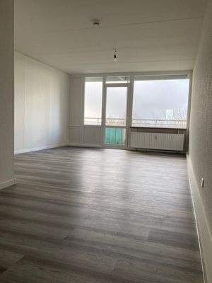 Wohnzimmer mit dunkelm Boden und ZUgang zum Balkon