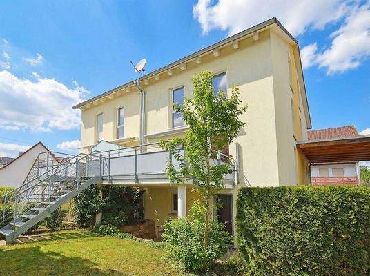 Hausansicht vom Garten mit überdachter Terrasse und großem Balkon