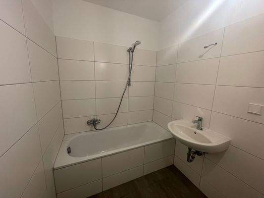 Badezimmer mit Badewanne und Waschbecken, weiß gefliest