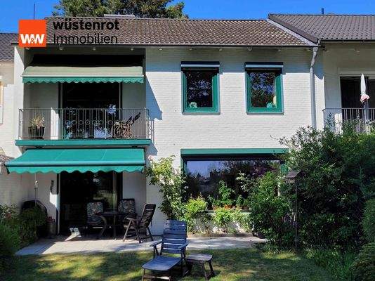 Blick vom Garten auf die Hausrückseite mit Balkon und die schöne Terrasse mit Außenmarkise