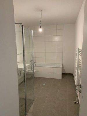 Badezimmer mit Dusche und Badewanne, weiß gefliest mit grauem Fliesenboden