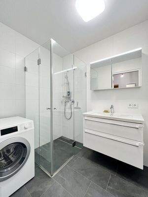 Modernes Bad mit Dusche, Waschbecken und Waschmaschinenanschluss