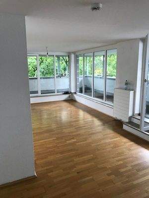 Wohnzimmer mit weißen Wänden und Parkettboden. Fenstertüren zum Balkon