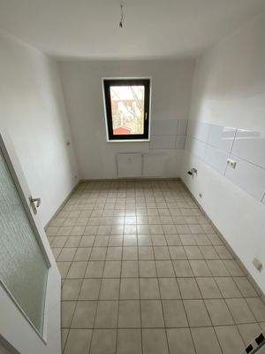 Küche mit hellen Bodenfliesen, weißen Wänden, weißem Fliesenspiegel und Fenster.jpg