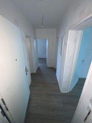 Flur mit weißen Wänden, weißen Zimmertüren und Designerboden in Holzoptik