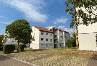 Wohnanlage mit mehreren  mehrstöckigen hellen Wohngebäuden, einem zentralen Gehweg der die Häuser miteinander verbindet und Grünflächen vor den Gebäuden