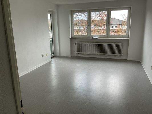 Wohnzimmer mit großer Fensterfront und Zugang zum Balkon, grauem PVC-Boden und weißen Wänden