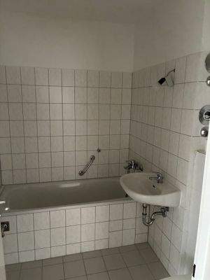 Badezimmer mit Wanne, weißen Sanitärobjekten, weiß-graue Wand- und Bodenfliesen