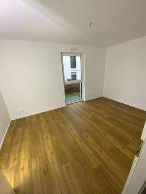 Schlafzimmer mit Vinylboden in Holzoptik, weißen Wänden und bodentiefem Fenster 