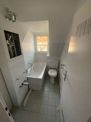 Badezimmer mit Tageslicht, weißer Badewanne, weißem Stand-WC und gräuliche Fliesen an Wand und Boden.jpg