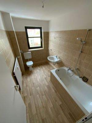 Tageslichtbad mit braunen Wandfliesen, weißem Stand-WC, weißter Badewanne und Wandwaschbecken und hellbraunem PVC Boden in Holzoptik.jpg