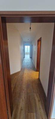 Rückansicht eines mehrstöckigen Wohngebäudes mit Garagen und Stellplätzen, umgeben von Bäumen und grünen Hecken.