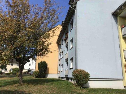 Rückansicht des mehrstöckigen Wohngebäudes mit Balkonen, umgeben von Grünanlagen mit Bäumen und grünen Sträuchern