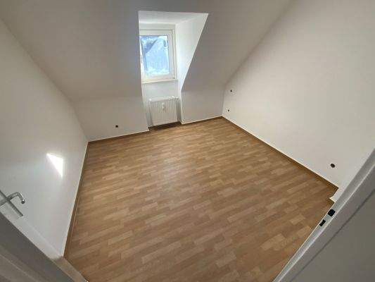 Schlafzimmer mit braunem PVC Boden, weißen Wänden, Dachschräge und Fenster.jpg