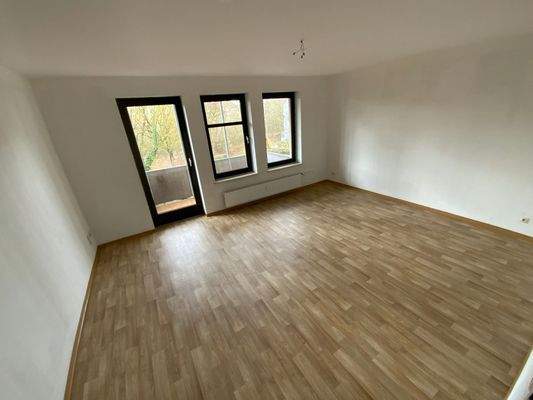 Wohnzimmer mit weißen Wänden, hellbraunem PVC Boden in Holzoptik, Fenster und Balkontür mit dunkelbraunem Rahmen.jpg