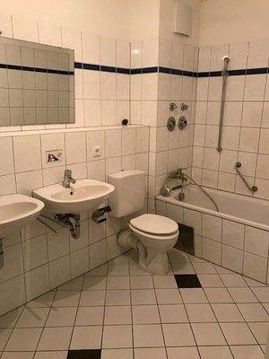 Bad ohne Tageslicht mit Badewanne und zwei Waschbecken. Weiße Wandfliesen, weißer Fliesenboden.JPG