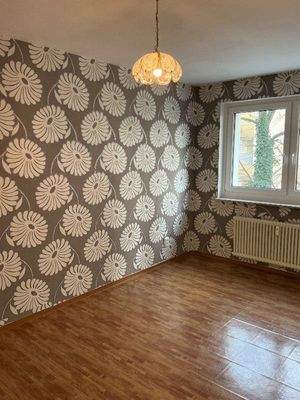 Schlafzimmer mit Fenster und geblümter Tapete.