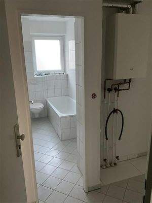 Blick vom Flur ins Badezimmer mit Badewann eund Hänge-WC, weiße Fliesen 