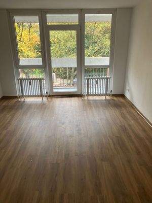 Wohnzimmer mit Design-Vinylboden in Holzoptik, weißen Wänden, sowie Zugang zum Balkon.