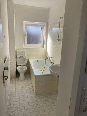 Bad mit Badewanne, weißen Sanitärobjekten, hellgelbem Fliesenspiegel und weiß-grauen Bodenfliesen