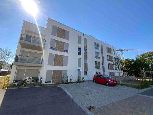 Vorderansicht des 4 stöckigen Wohngebäudes mit Balkonen links, davorstehende Stellplätze.JPG