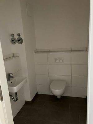 Gäste-WC mit weißen Sanitärobjekten, weißem Fliesenspiegel und dunkelgrauen Bodenfliesen