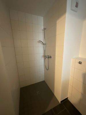 Ansicht der Dusche im Bad; weiße Wandfliesen und dunkelgraue Bodenfliesen