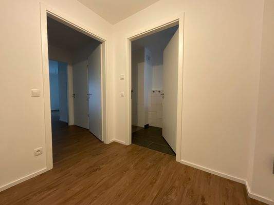 Beispielhafte Wohnung: Flurbereich mit Blick Richtung Wohnzimmer und Bad; weiß angelegte Wände und brauner Vinyl-Designboden in Holzoptik