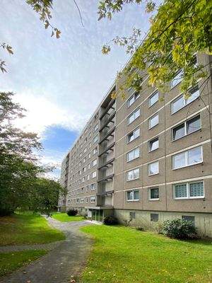 Seitenansicht eines mehrgeschossigen Wohnhauses mit Eingang und Bepflanzung