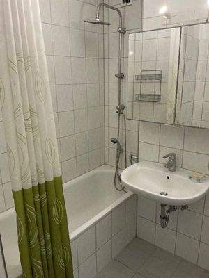 Badezimmer mit weiß grauen Boden- und Wandfliesen, Badewanne, Handwaschbecken und Spiegelschrank