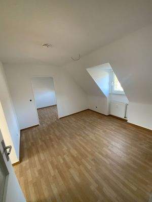 Wohnzimmer mit braunem PVC Boden, weißen Wänden, Dachschräge und Fenster.jpg