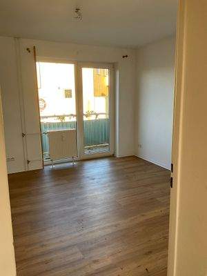 Wohnzimmer mit braunem Vinylboden. Decken und Wände weiß angelegt. Mit Zugang zum Balkon.